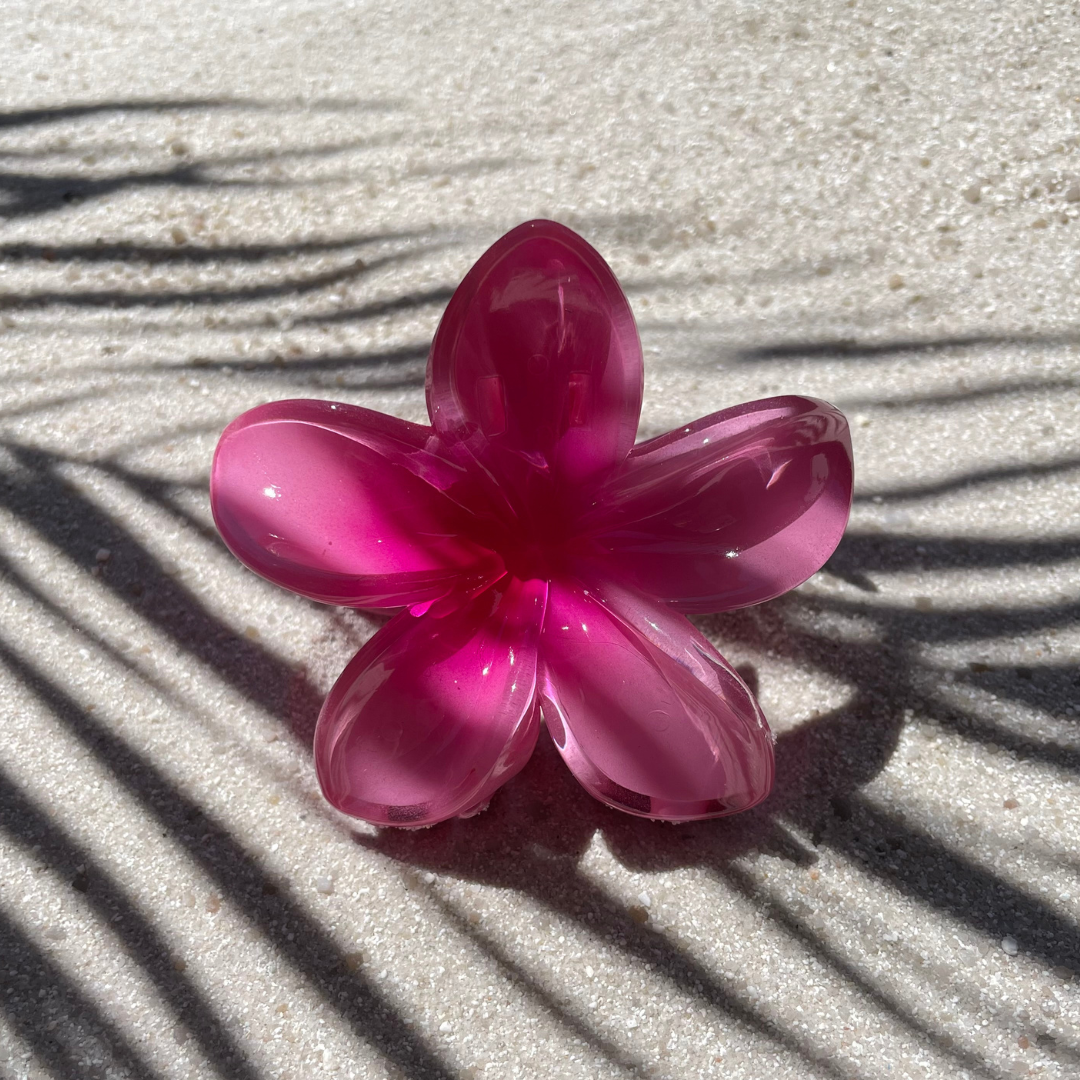 Blumenförmige Haarklammer in Rosa mit pinkem Farbverlauf in der Mitte, arrangiert auf sandigem Untergrund im Sonnenlicht. Die Klammer erinnert an eine tropische Blüte und sorgt für einen sommerlichen Akzent im Haar. 